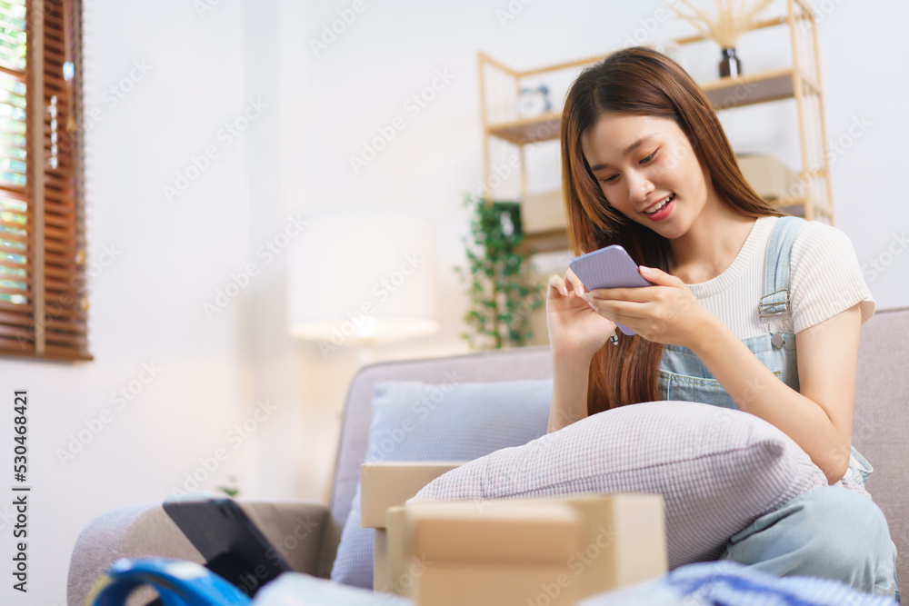 Online seller concept, Female entrepreneur checks online orders on smartphone to prepare parcel box Online seller concept, Female entrepreneur checks online orders on smartphone to prepare parcel box