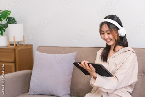 Lifestyle at home concept, Young Asian woman is listening music and surfing social media on tablet