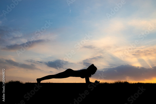 The slender girl is doing a yoga warm-up exercise outdoors