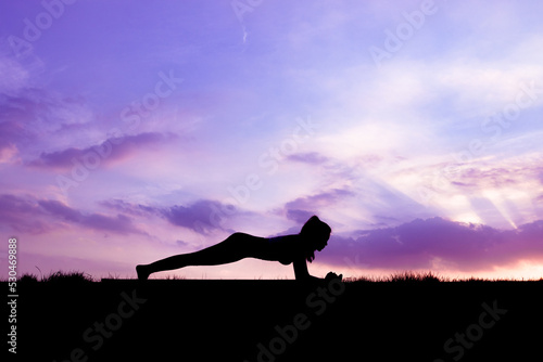 The slender girl is doing a yoga warm-up exercise outdoors © Mulin