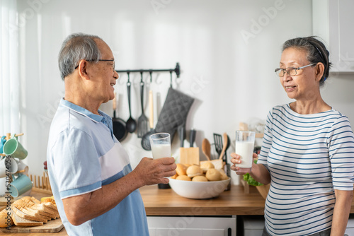Asian senior elderly couple drink a glass of milk in kitchen at home. 