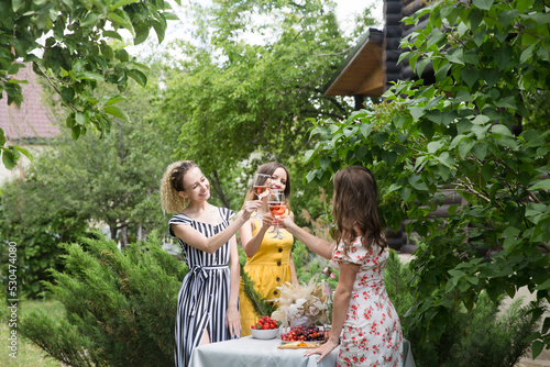 three  young beautiful smiling woman have fun together and drink wine in the summer garden   female friends enjoying a holiday outdoors