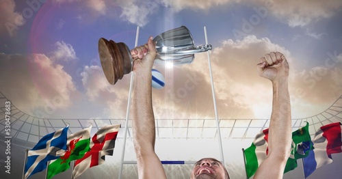 Composition of male rugby player celebrating victory, holding trophy on rugby pitch at stadium