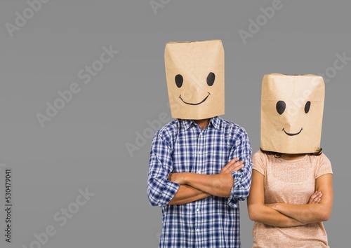 Couple wearing paper bags with face emotions painting against copy space on grey background