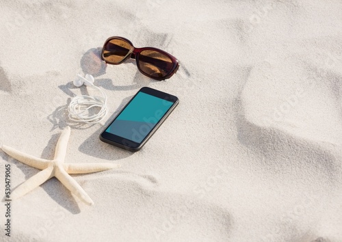 Smartphone, sunglasses, earphones and star fish on sand at the beach with copy space