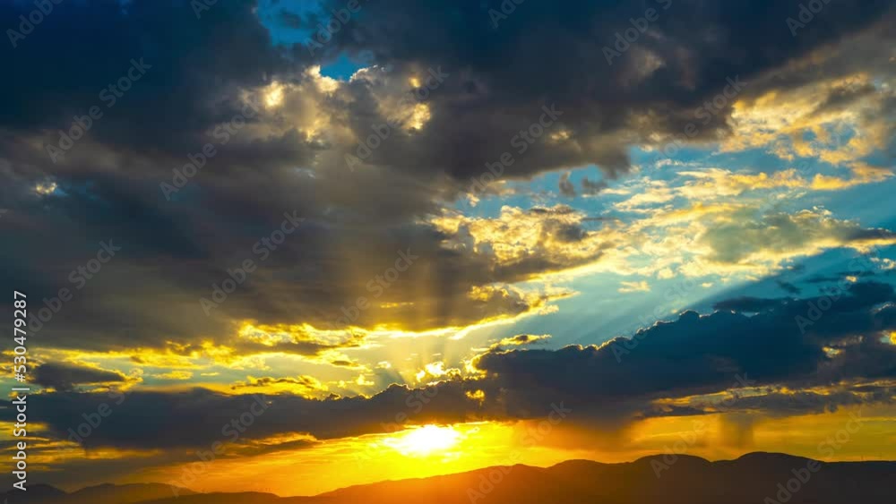 Colorful golden sunrise over the silhouette of the Mojave Desert mountains with sunbeams shining through the stormy clouds - time lapse Colorful golden sunrise over the silhouette of the Mojave Desert mountains with sunbeams shining through the stormy clouds - time lapse