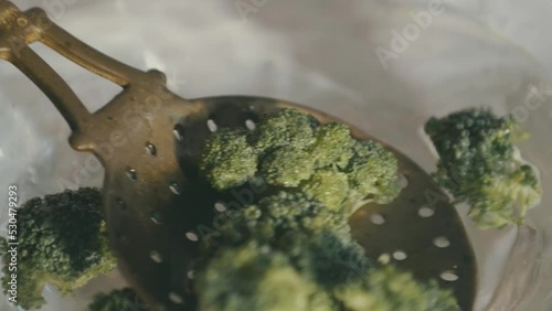 An old ladle with holes in it scoops broccoli out of the water and carries it towards the chamber, impaling it photo