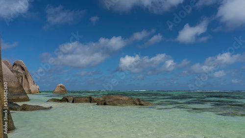 There are giant rounded boulders on the beach and in the ocean. Clear turquoise water and blue sky with clouds. Seychelles. La Digue Island. Anse Source D’Argent beach