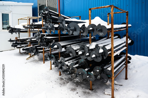 Helical piles on rusty metal rack in snowy warehouse yard
