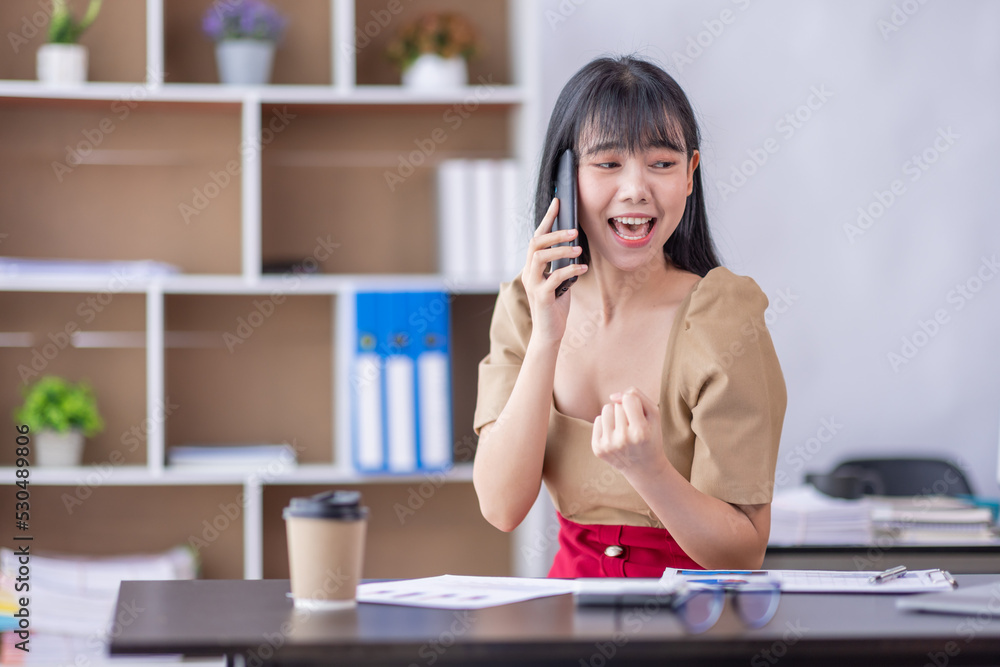 Excited happy Business Asian woman talking on phone and celebrating an online win, overjoyed young asian female screaming with joy and working at workplace Excited happy Business Asian woman talking on phone and celebrating an online win, overjoyed young asian female screaming with joy and working at workplace
