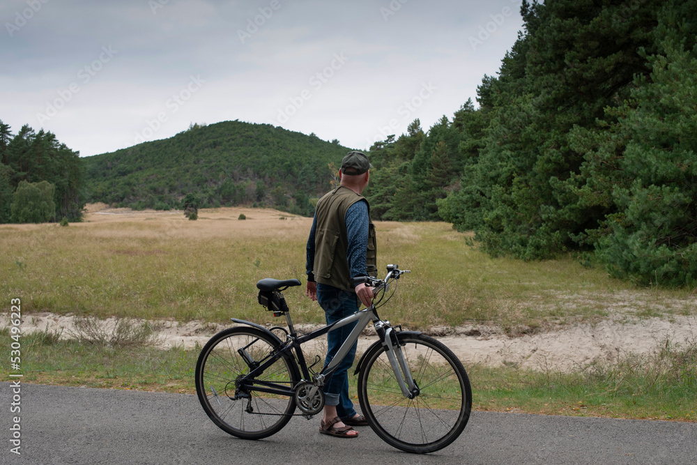 A man with bicycle on recreational cycle path looking at the hill. A man with bicycle on recreational cycle path looking at the hill.