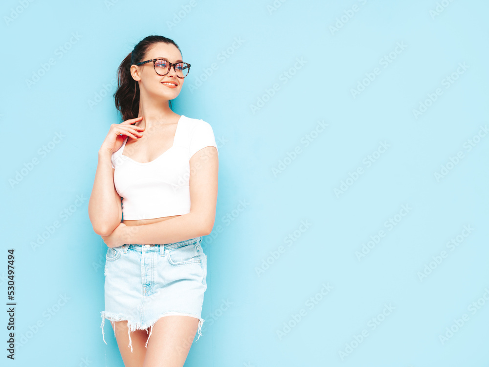 Young beautiful smiling female in trendy summer jeans skirt and top clothes. carefree woman posing near blue wall in studio. Positive brunette model having fun.Cheerful and happy Young beautiful smiling female in trendy summer jeans skirt and top clothes. carefree woman posing near blue wall in studio. Positive brunette model having fun.Cheerful and happy