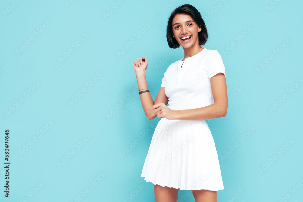 Young beautiful smiling female in trendy summer white top and skirt. Carefree woman posing near blue wall in studio. Positive model having fun indoors. Cheerful and happy. Celebrating and dancing Young beautiful smiling female in trendy summer white top and skirt. Carefree woman posing near blue wall in studio. Positive model having fun indoors. Cheerful and happy. Celebrating and dancing