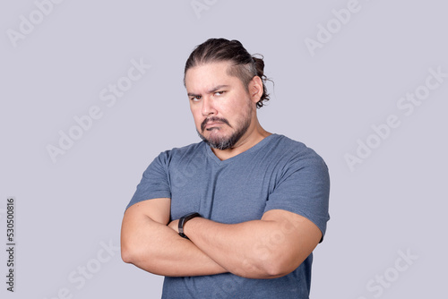 A bitter man in his 30s looks at the camera with a scowling face and arms crossed. Jealousy, displeasure or pettiness.