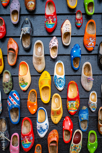 Old wooden Dutch shoes - klomps. A lot of colorful old clomps against the background of a wooden wall. Popular souvenirs. Traditions of Holland. Background