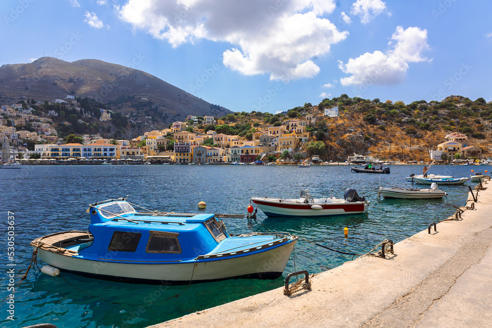 Panoramic view of small haven of Symi island. Village with tiny beach, moored boats and colorful houses located on rock. Tops of mountains on Rhodes coast, Greece