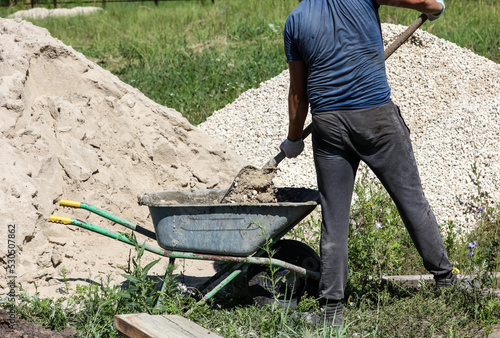 A worker kneads a mixture of concrete in a wheelbarrow at a construction site.