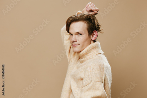 portrait of a handsome redhead guy with freckles in a fluffy beige sweater posing with his hand on his head