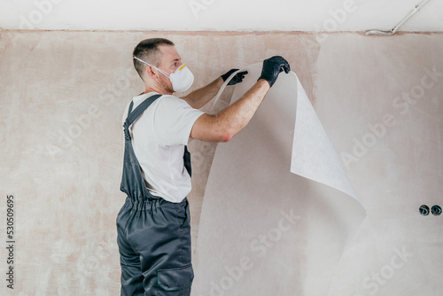 Foto Male worker in coveralls applying fiberglass surface tissue on the wall
