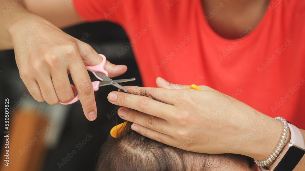 Obraz premium Asian Mother cutting her Little son's hair at home outdoor, Adorable boy having fun.