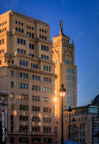Sun burst reflecting of ornate facades of beautiful buildings near Gran Via shopping streets in the center of the city in Madrid, Spain at sunset