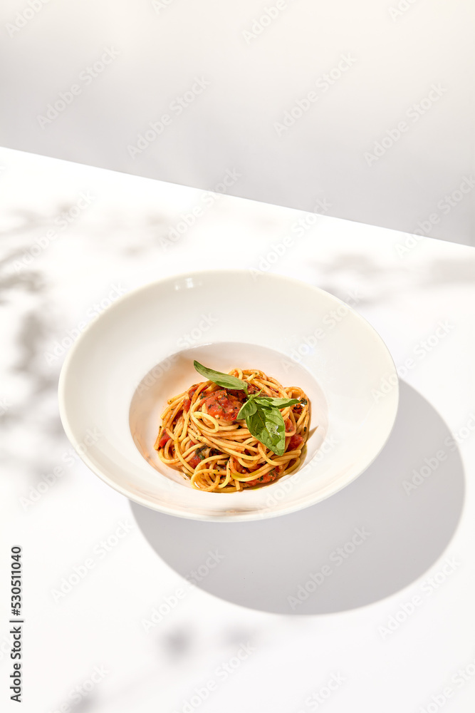 Vegetarian pasta with basil and tomatoes on white plate. Tomato pasta in summer menu with hard shadows Spaghetti with tomatoes on light background. Vegan food - spaghetti marinara Vegetarian pasta with basil and tomatoes on white plate. Tomato pasta in summer menu with hard shadows Spaghetti with tomatoes on light background. Vegan food - spaghetti marinara
