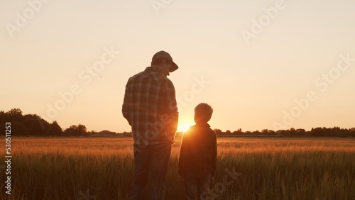 Farmer and his son in front of a sunset agricultural landscape. Man and a boy in a countryside field. Fatherhood, country life, farming and country lifestyle. photo