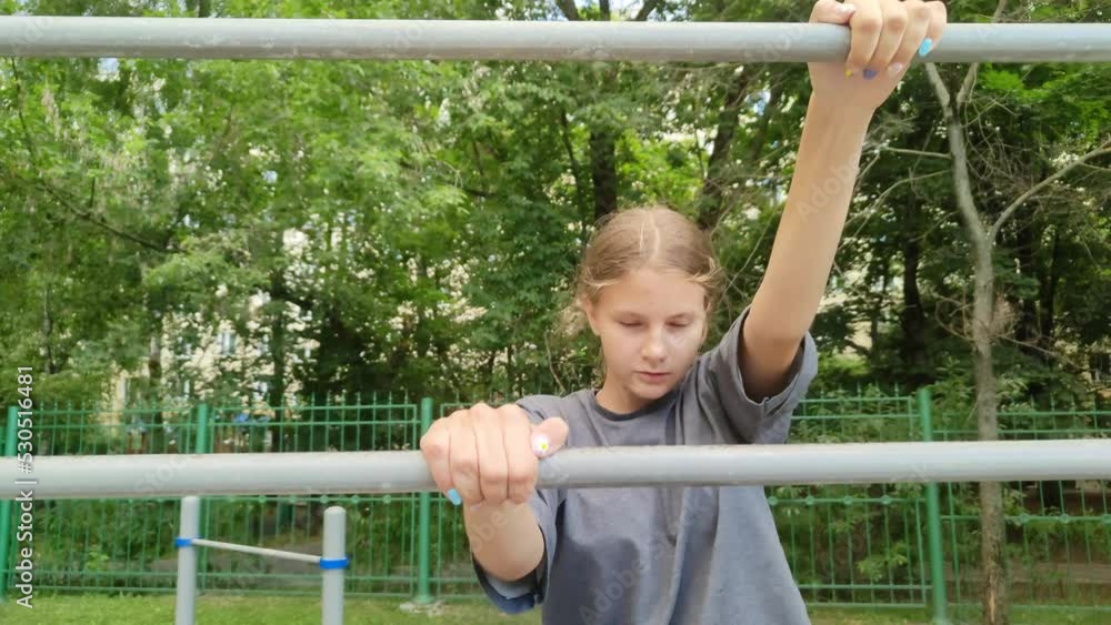 Beautiful teen girl with blonde hair climbs up a metal ladder. Wall bars on the playground in the city park. Child is playing on the playground near the school. Horizontal bars for sports activities Beautiful teen girl with blonde hair climbs up a metal ladder. Wall bars on the playground in the city park. Child is playing on the playground near the school. Horizontal bars for sports activities