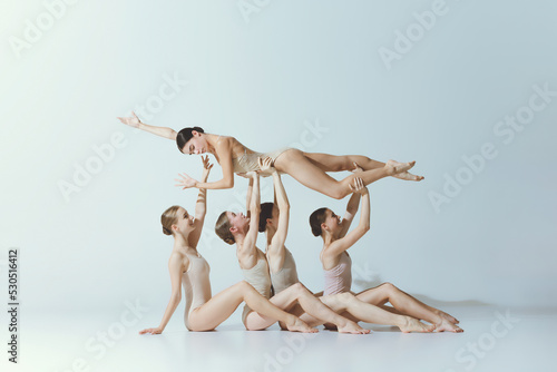 Group of young girls, ballet dancers performing, posing isolated over grey studio background. Lying on hands