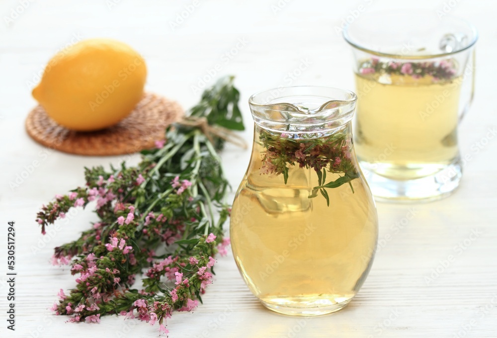 Herbal tea from pink fresh flowers of hyssopus, lat. Hyssopus officinalis in a jug and glass on white wooden table. Aromatic hyssopus tea is used in traditional herbal medicine. Herbal tea from pink fresh flowers of hyssopus, lat. Hyssopus officinalis in a jug and glass on white wooden table. Aromatic hyssopus tea is used in traditional herbal medicine.