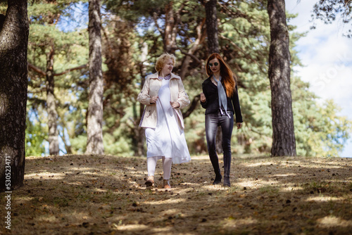 Two women together - blonde in light and redhead in dark clothes - walking in a forest. Cosplay - female version of Angel and Demon (Good Omens)