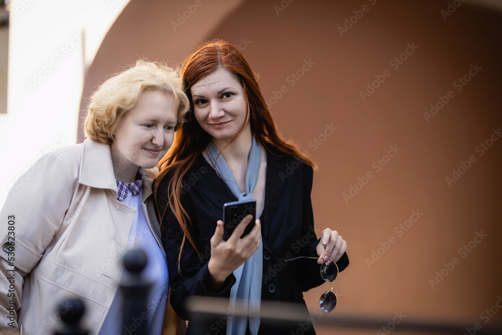 Two women together - blonde in light and redhead in dark clothes with a smartphone. Cosplay - female version of Angel and Demon (Good Omens) Two women together - blonde in light and redhead in dark clothes with a smartphone. Cosplay - female version of Angel and Demon (Good Omens)