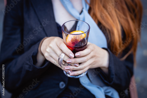 Female hands hold a transparent cup with mulled wine, close-up