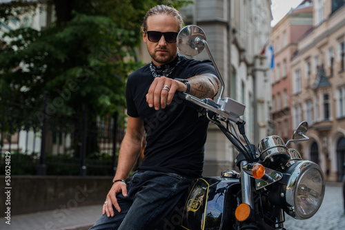 Shot of man biker with his custom motorcycle at street in alley looking at camera.