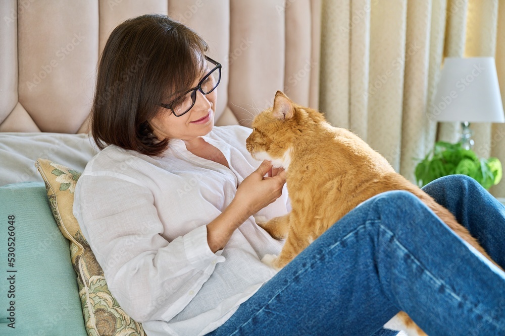 Middle aged woman talking with ginger pet cat, home interior background Middle aged woman talking with ginger pet cat, home interior background