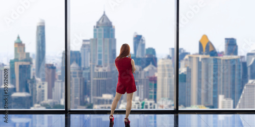 Luxury young Asian CEO woman entrepreneur looking at the downtown skyline at the window with skyscraper and cityscape for vision and real estate development
