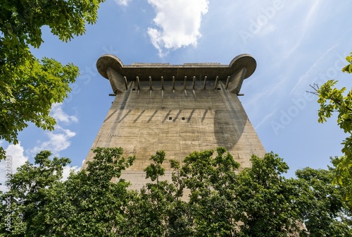 Vertical shot of a Flak tower surrounded by trees under the cloudy blue sky in Vienna, Austria photo