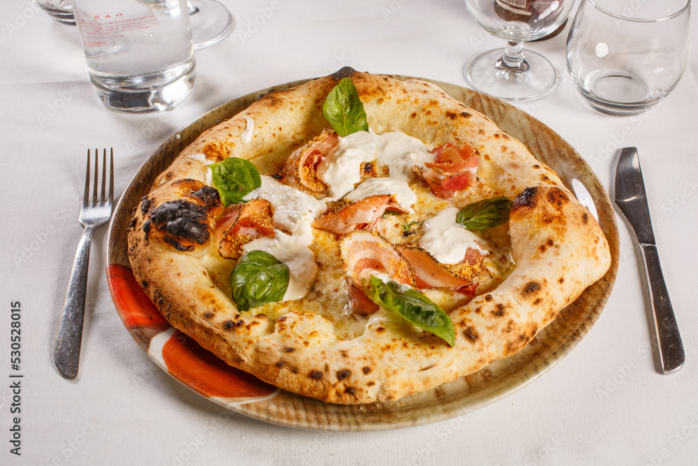 Pizza napoletana con mozzarella, pancetta, mozzarella, tarallo napoletano e basilico fresco servita in una pizzeria