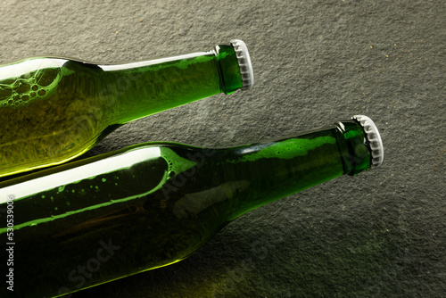 Image of two green glass beer bottles with white crown caps lying on slate, with copy space