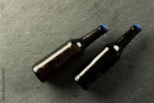 Image of two dark beer bottles with blue crown caps lying on slate, with copy space