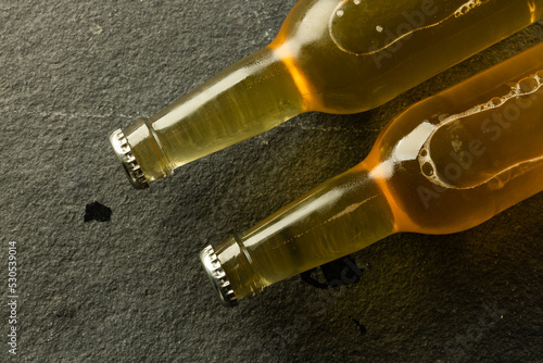 Image of two clear glass beer bottles with crown caps lying on slate, with copy space