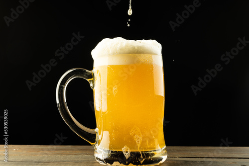 Image of beer pouring into glass tankard of foamy beer on wooden table, with copy space