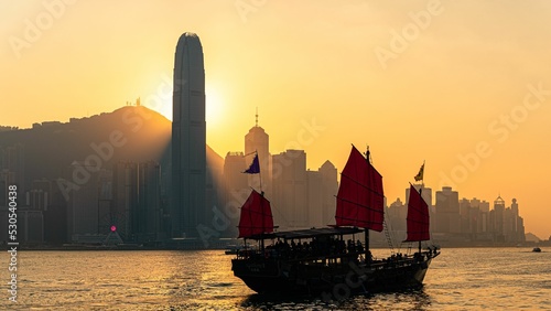 Photography Silhouette of a traditional boat near a modern Asian city on the sunset