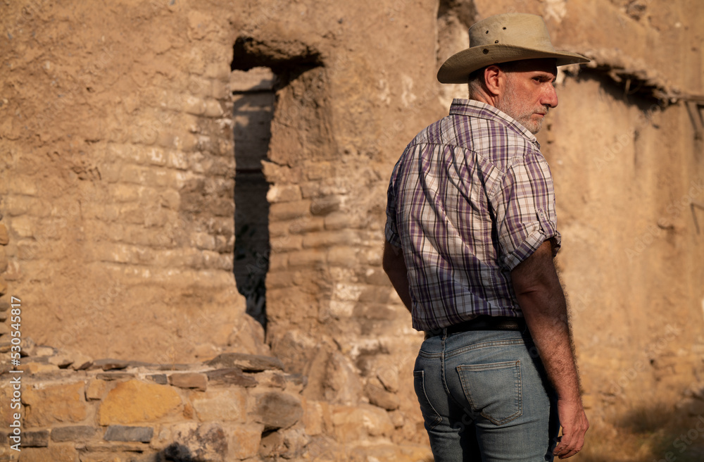 Rear view of adult man in cowboy hat and shirt against abandoned building Rear view of adult man in cowboy hat and shirt against abandoned building