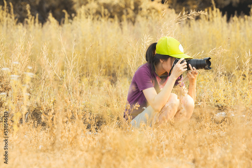 Woman photographer with dslr camera, with sunset warm tone in the meadow field