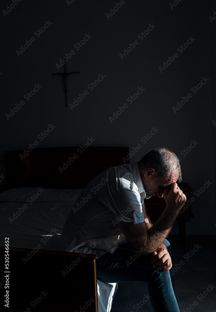 Portrait of adult man sitting on bed against window with sunlight and shadow