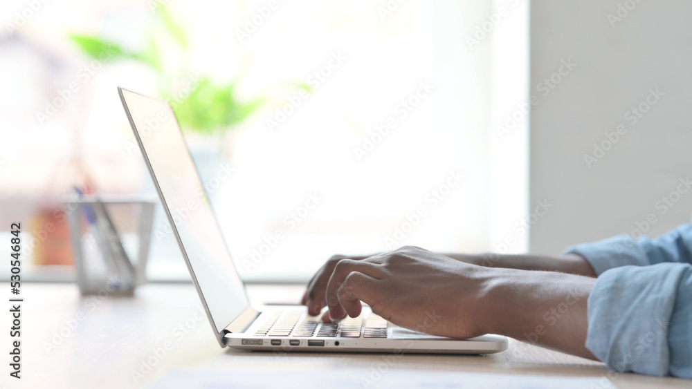 Side View of Young African Man Typing on Laptop Keyboard Side View of Young African Man Typing on Laptop Keyboard