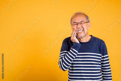 Dental pain. Portrait senior old man sad hand touching cheek suffering from toothache studio shot isolated on yellow background, Asian unhappy elder man problems with teeth pain, dental healthcare © sorapop