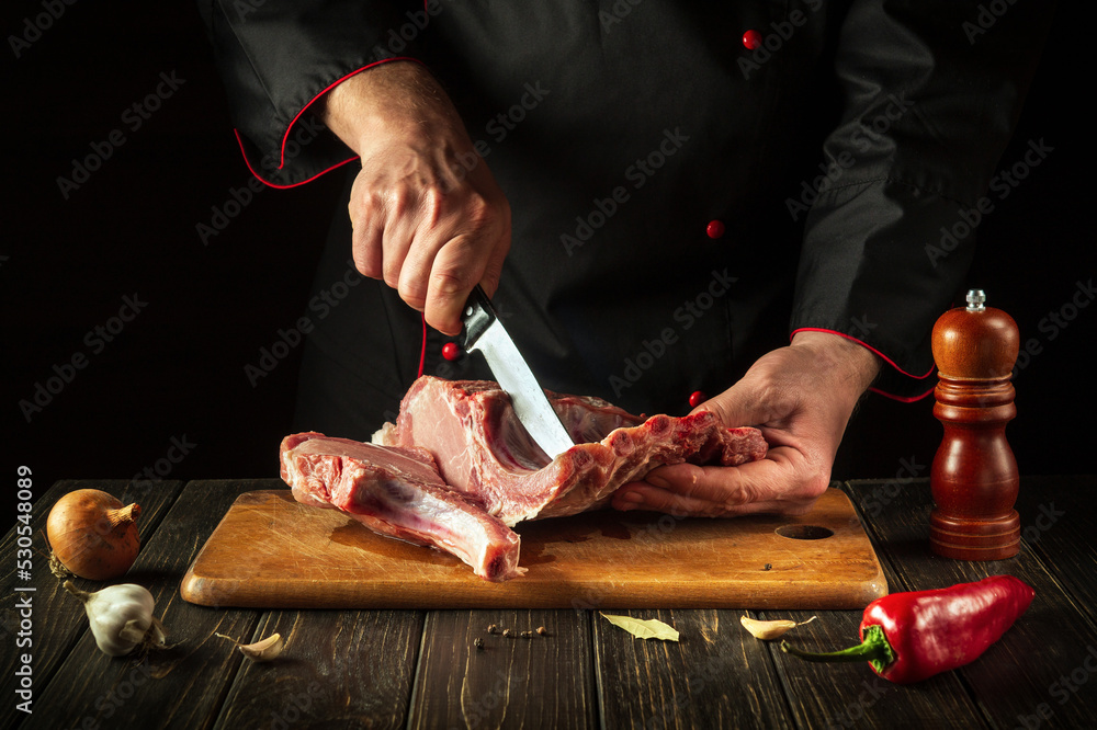 Professional chef cuts raw meat. Butcher cutting pork ribs. Meat with bone on a wooden cutting board.