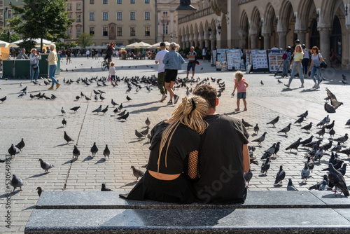 Couple sitting on a marble bench outdoors in the city square on a sunny summer day, traditional young couple, tourists in Krakow, close relationship, love